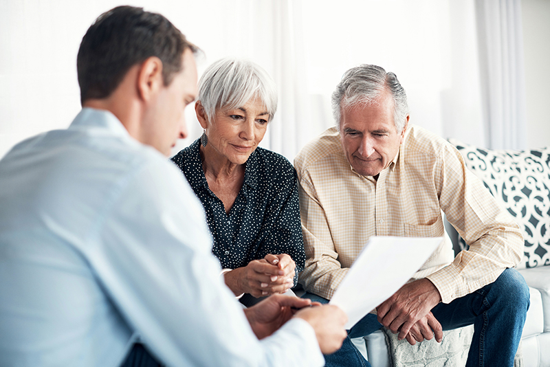 Senior-aged couple reviewing financial paperwork with financial representative